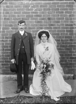Wedding portrait, showing a bride and groom, with a brick wall behind, possibly Christchurch district