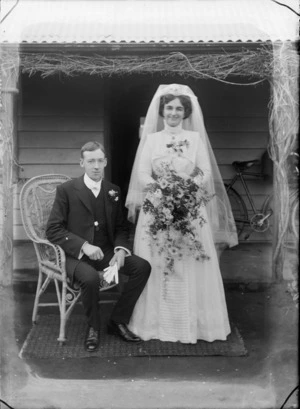 Wedding portrait, showing an unidentified bride and groom, with entrance to a domestic wooden building behind, including a bicycle on verandah, possibly Christchurch district