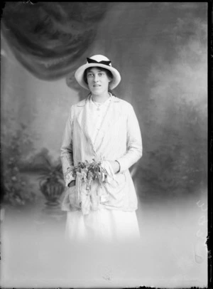 Studio portrait of unidentified young woman wearing a hat and necklace and holding a posy, probably Christchurch district