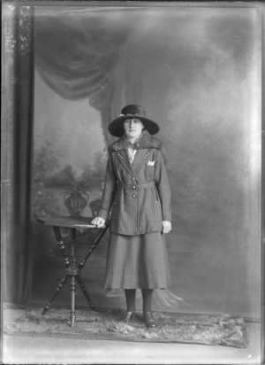 Studio portrait of an unidentified woman leaning on a table, wearing a hat and pinned striped suit and a fur capelet, probably Christchurch district