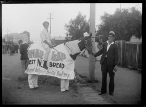 Boy on horse dressed as a baker, with advertising banner 'Phar Lap, Best NZ Bread, Delivered Daily by the Betta Bakery', with man holding the reins for a parade, Hastings, Hawke's Bay District