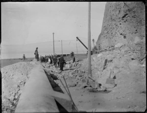 Napier earthquake damage, view of large rock fall covering road and onto the beach, with group of people looking on, port area, Napier City, Hawke's Bay District
