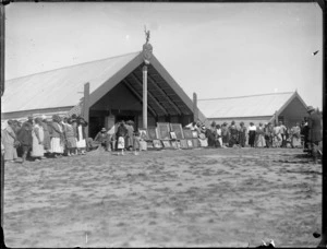 Gathering in front of meeting houses, Omahu Marae, with portraits and photos of family members, Fernhill, Hastings, Hawke's Bay District