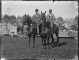 Two older men [Neilson?] on horses at the Haumoana Show, cars and horse trailer behind, Haumoana, Hawke's Bay District