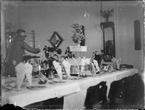 Wedding reception, with a maid doing final touches prior to guests arriving, wedding cake on table, Hawke's Bay District