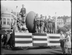 New Napier Week Carnival, float with a rugby theme featuring an All Black player with other younger players, with large rugby ball and small goal posts, Napier, Hawke's Bay District