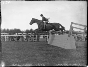 Autumn Show, showing Freda White on a black horse jumping a wooden fence, spectators beyond, Hawke's Bay District