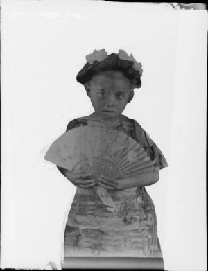 Portrait, masked photo of a small Maori girl holding a fan, and wearing a dress with cut out paper flowers an plant patterns, Hawke's Bay District