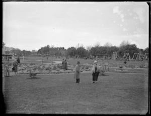 Women walking around a park, with children playing on swings in the background, Hawke's Bay District