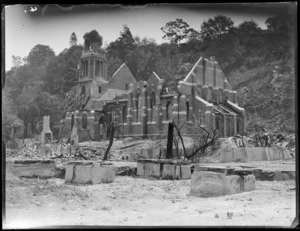 Napier Earthquake, view of a destroyed church, steeple gone, with makeshift supports on its walls and neighbouring building burnt by fire and hillside beyond, Napier, Hawke's Bay District