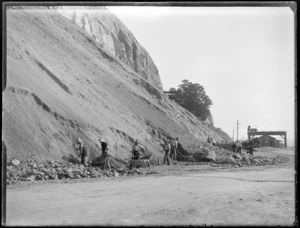 Napier Earthquake, view of men working to remove slip debris covering Breakwater Road below Bluff Hill, wharf area beyond, Napier, Hawke's Bay District