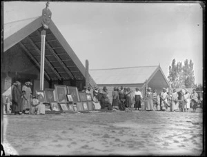 Gathering in front of meeting houses, Omahu Marae, with portraits and photos of family members, women with fresh branches and leaf headbands, Fernhill, Hastings, Hawke's Bay District