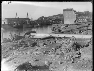 Napier Earthquake, view of damaged dock area retaining wall and collapsed building in foreground, fishing boat tied up at wharf with warehouses and Bluff Hill residential area beyond, Napier, Hawke's Bay District