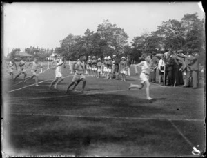 View of the winner of a primary school boys running race crossing the line and taking the tape, spectators and officials look on, Hawke's Bay District