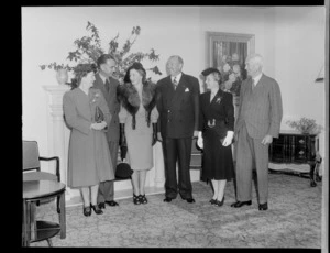 Group of unidentified men and women, in a formally decorated room with fireplace, location unidentified