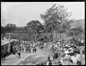 Spectators and cyclists gathered for an unknown event at the junction of two roads, unidentified location