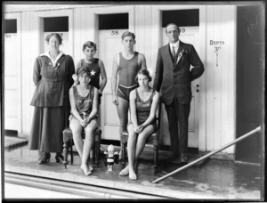 Two unidentified adults and four young swimmers with kewpie dolls beside an unidentified swimming pool; the two female swimmers have Te Awa on their singlets