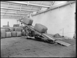 New Zealand Loan & Mercantile Agency Company Ltd wool and grain stores, with two large bales of wool on a conveyor belt, with sheepskins on the floor on the right and bales of wool in the background