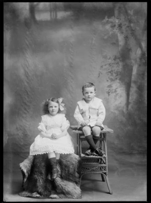 Studio unidentified family portrait with a young girl in a lace dress sitting on fur rug covered chair next to her younger brother in a sailor's outfit sitting on a cane table, Christchurch