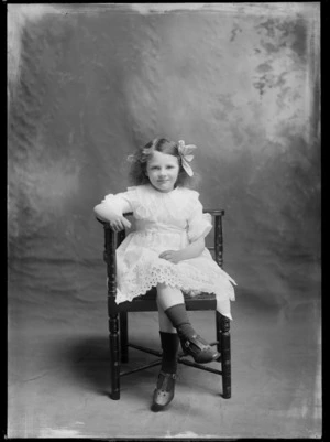 Studio unidentified family portrait of a young girl in a lace dress with a large collar, belt and hair bow, sitting on a wooden chair, Christchurch