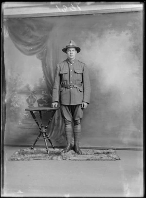 Studio portrait of unidentified young World War One soldier in uniform with bird collar badges and hat with black band and silver fern crown badge, Christchurch