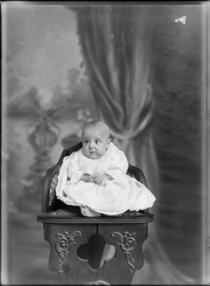 Studio family portrait of an unidentified young baby in christening gown sitting on wooden high chair, Christchurch