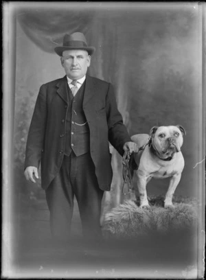 Studio portrait, unidentified older man with moustache, striped tie and hat, standing holding leash of a bulldog on a fur rug, Christchurch