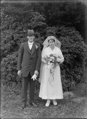 Unidentified outdoor wedding portrait with bride in veil, and groom with black armband, carnation, gloves and hat, probably Christchurch region