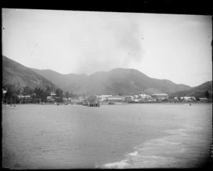 View of Picton Harbour, showing wharf, waterfront buildings, and small boats, with hills in distance