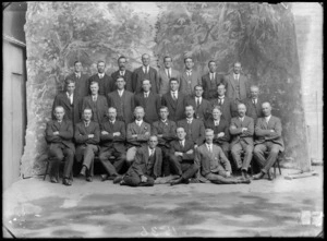 Studio portrait of a large group of unidentified men, all wearing business attire, with painted backdrop of trees
