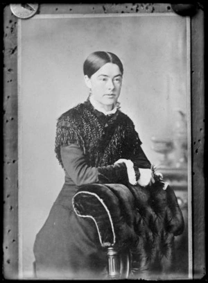 Studio portrait of an unidentified young woman, leaning on the back of a upholstered velvet chair