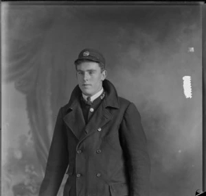 Studio portrait of an unidentified man, dressed in a tram conductor uniform and cap, showing the partially obscured badge [Conductor?] on his left collar, possibly Christchurch district