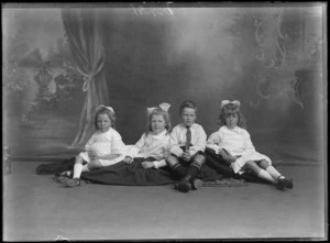 Studio portrait of an unidentified family of three girls wearing bow ribbons in their hair and a boy sitting on cushions, possibly Christchurch district