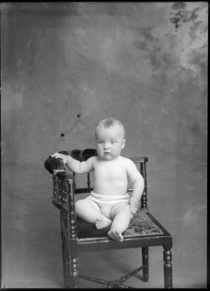 Studio portrait of an unidentified baby wearing a knitted undergarment, sitting on a chair