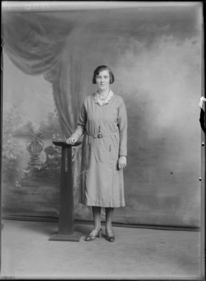 Studio portrait of an unidentified woman standing next to a wooden stand, resting her hand on it, possibly Christchurch district