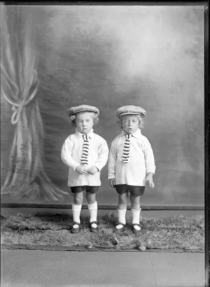 Studio portrait of unidentified [twin?] boys dressed in dark shorts, long sleeved white shirts with a striped tie and caps, possibly Christchurch district