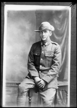 Studio portrait of unidentified young soldier sitting against a table wearing slouch hat, and with silver fern badges on collars, Christchurch