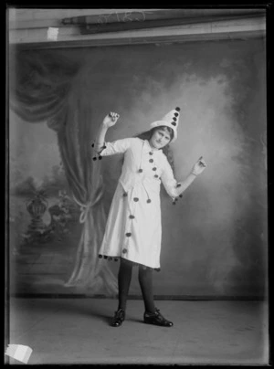Studio wedding portrait of unidentified young woman with long hair in clown costume and hat with small pompoms striking a pose, Christchurch