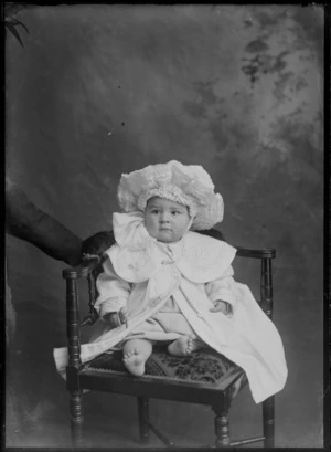 Studio portrait, unidentified baby sitting on chair in embroidered christening gown with large collar and bar brooch and large lace bonnet, Christchurch