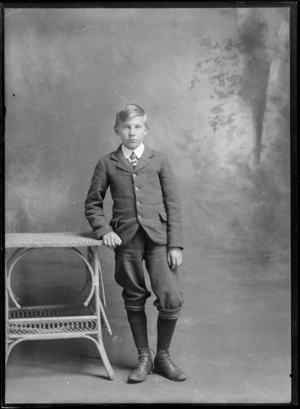 Studio family portrait of unidentified older boy in a suit and double round shirt collar and tie, with his socks pulled up to his knees, Christchurch