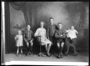 Studio portrait of six unidentified children, includes three boys, two girls and a baby seated on a carved wooden chair, probably Christchurch district