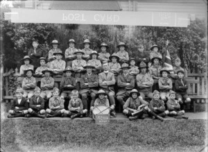 Saint Saviour's Boy Scouts Troop outdoors, unidentified boys and adult men in scout uniforms, with Anglican Priest, bugle, drum and flag, 30 Oct 1920 sign, probably Christchurch district