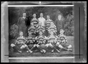 Outdoors portrait on grass with trees behind of unidentified men's [soccer?] football team, with player in uniform with boots, two coaches and ball, probably Christchurch region
