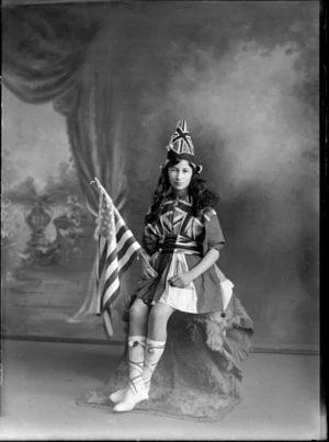 Studio portrait of unidentified girl, dressed in Union Jack flags and holding an American flag, probably Christchurch district