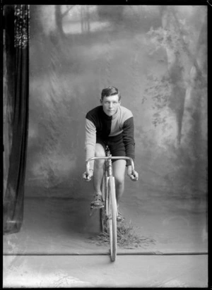 Studio portrait of unidentified male cyclist in uniform, sitting on a racing bicycle, probably Christchurch district