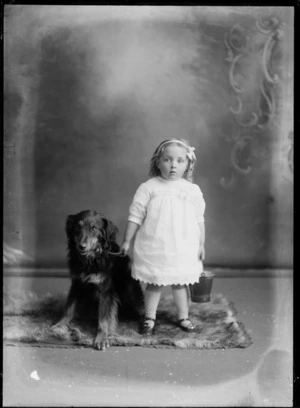 Studio family portrait, an unidentified small girl in lace cotton dress with googly eye shoes, standing with small tin bucket and large dog, Christchurch