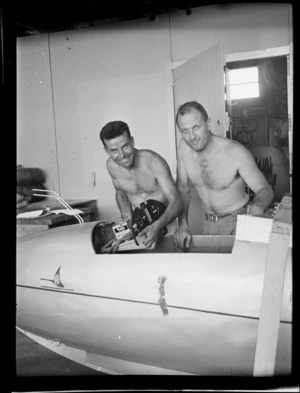 Two topless Auckland Gliding Club members, G Hookings and A Vause (left to right), fixing the steering mechanism in a glider aircraft, Mangere Aerodrome, Manukau City, Auckland Region