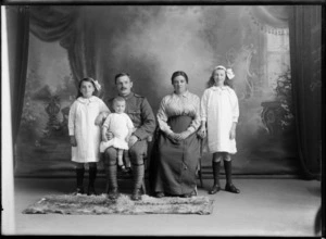 Studio unidentified family portrait, a World War I soldier with moustache and toddler daughter on his knee, sitting alongside his wife and two older daughters with hair bows and lockets standing, Christchurch