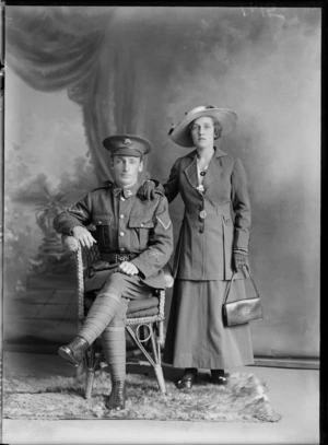 Studio unidentified family portrait, a Lance Corporal World War I soldier with native bird collar and hat badges and sleeve gun insignia, and wife with portrait and bird brooches, hat, gloves, handbag and bracelets, Christchurch
