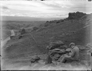 Unidentified man sitting on a rock looking over the landscape outside Alexandra, Central Otago